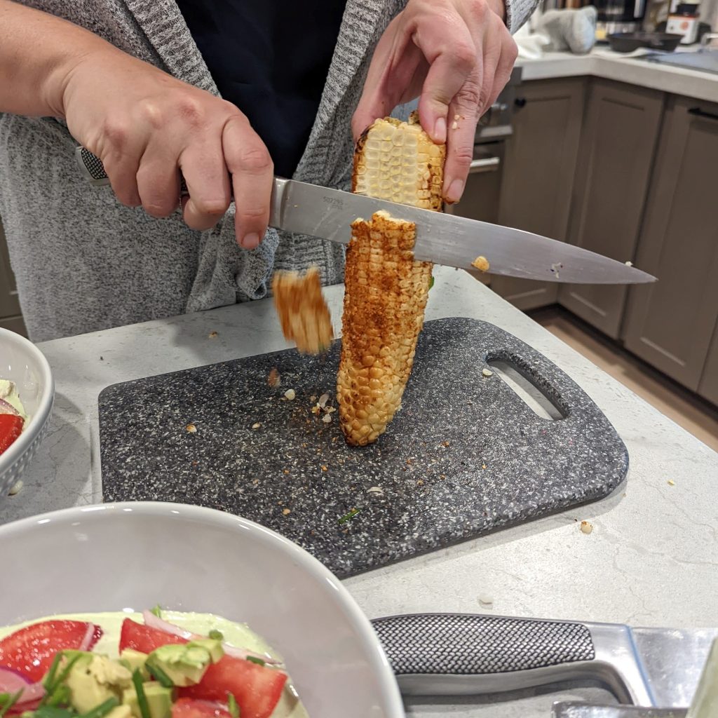 Image cutting corn off of corn to make green garden salad.